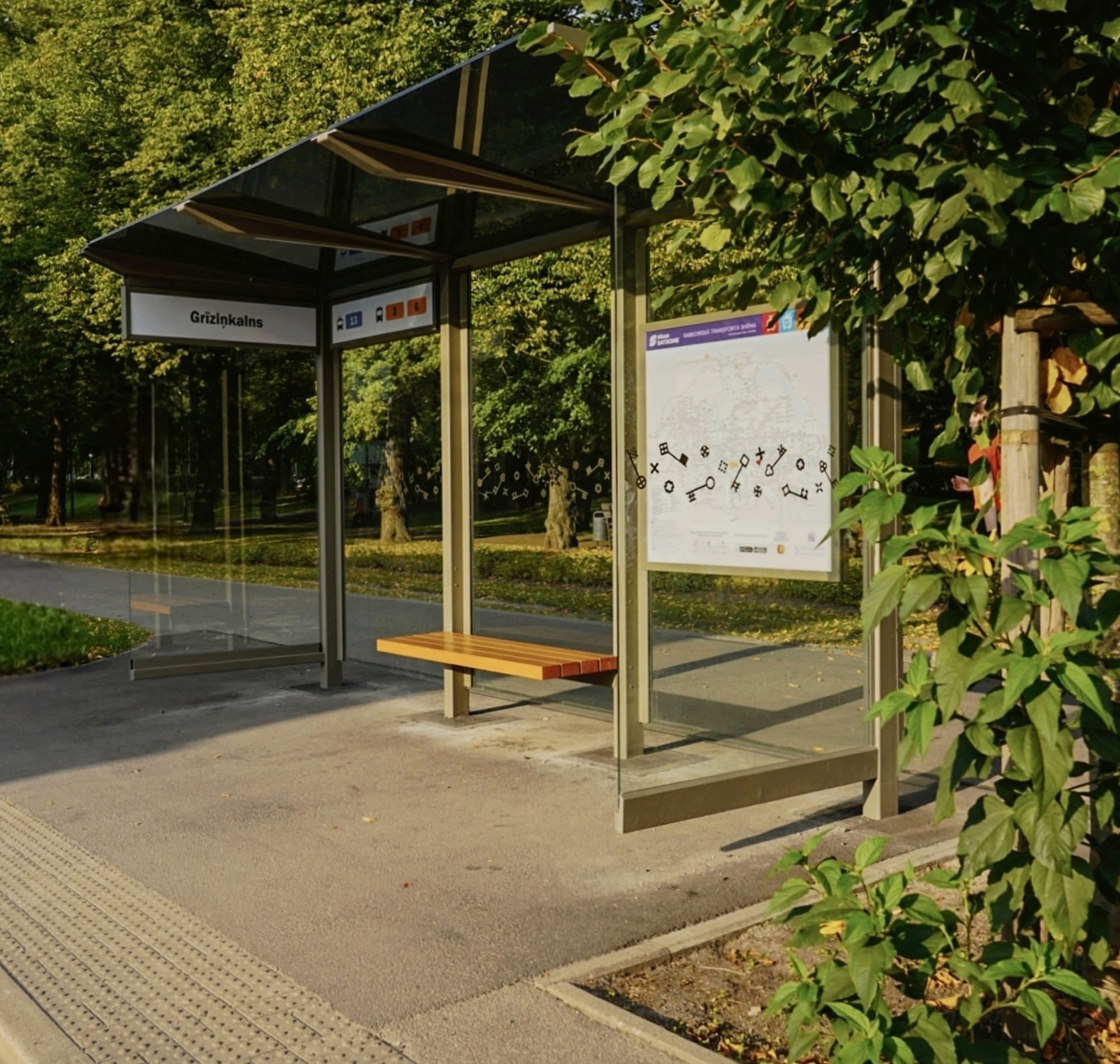 Bus shelter with a bench and information board on street with trees