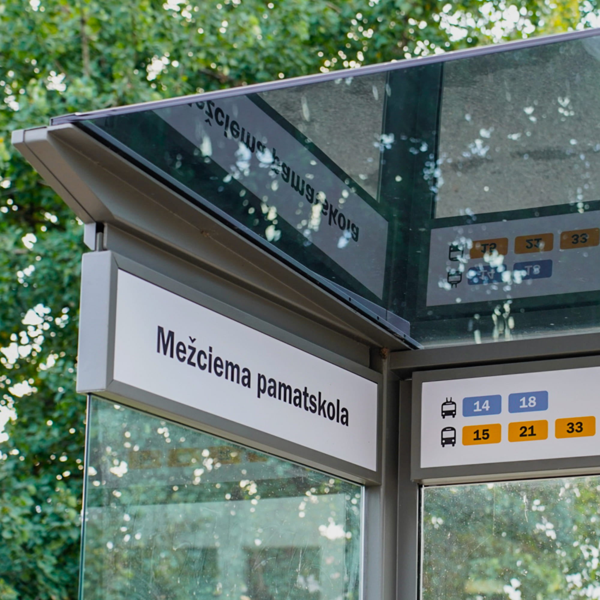 Bus stop shelter with electronic display and route information against a green tree background